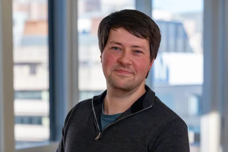 Photo of Professor Cameron Werner, a white man with brown hair. He is wearing a blue t-shirt under a zip up top.