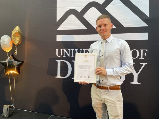 a man collects a civic award from the university of derby