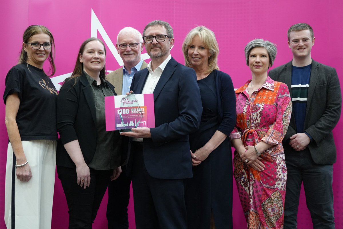 Group of lecturing staff receiving a trophy on stage with a pink background.