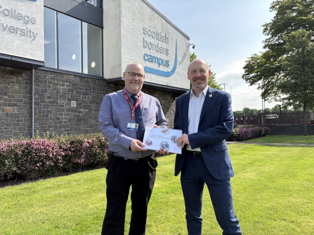Photo of two borders college employees standing outside the scottish borders campus holding a booklet