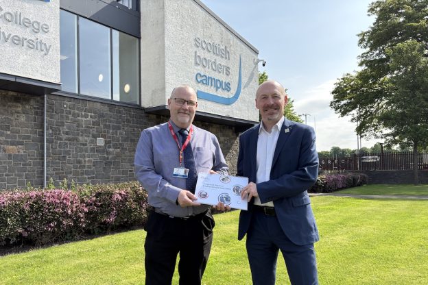 Photo of two borders college employees standing outside the scottish borders campus holding a booklet