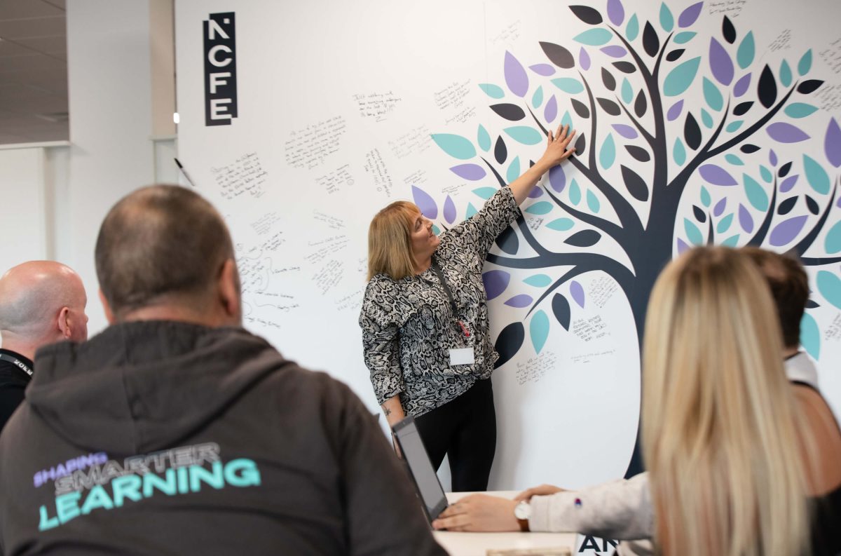 NCFE colleagues sit and watch as another colleague points to a board with an illustration of a tree