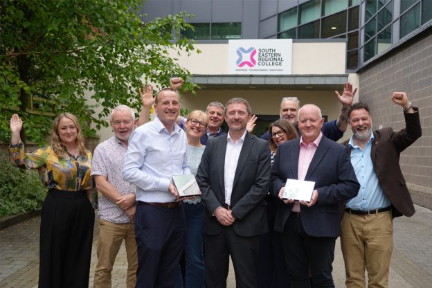 Group of male and female lecturers outside college holding Awards and cheering.