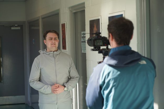 Man wearing grey tracksuit standing in front of camera