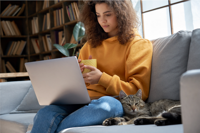 Lady sat on sofa looking at laptop while drinking coffee