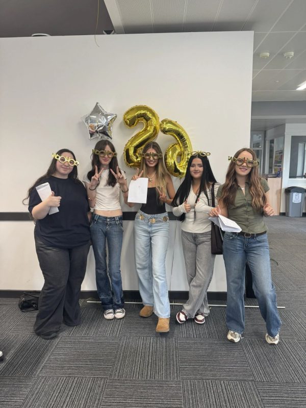 Students are standing together in the Llangefni campus in front of gold balloons.