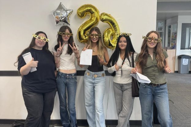 Students are standing together in the Llangefni campus in front of gold balloons.