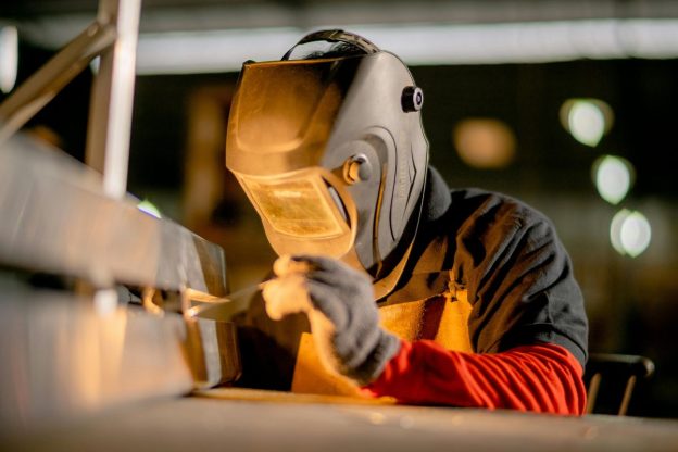 Welder in protective helmet and gloves working on a metal section in a workshop