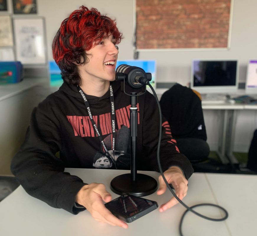 A student sits in front of a microphone to present a radio show